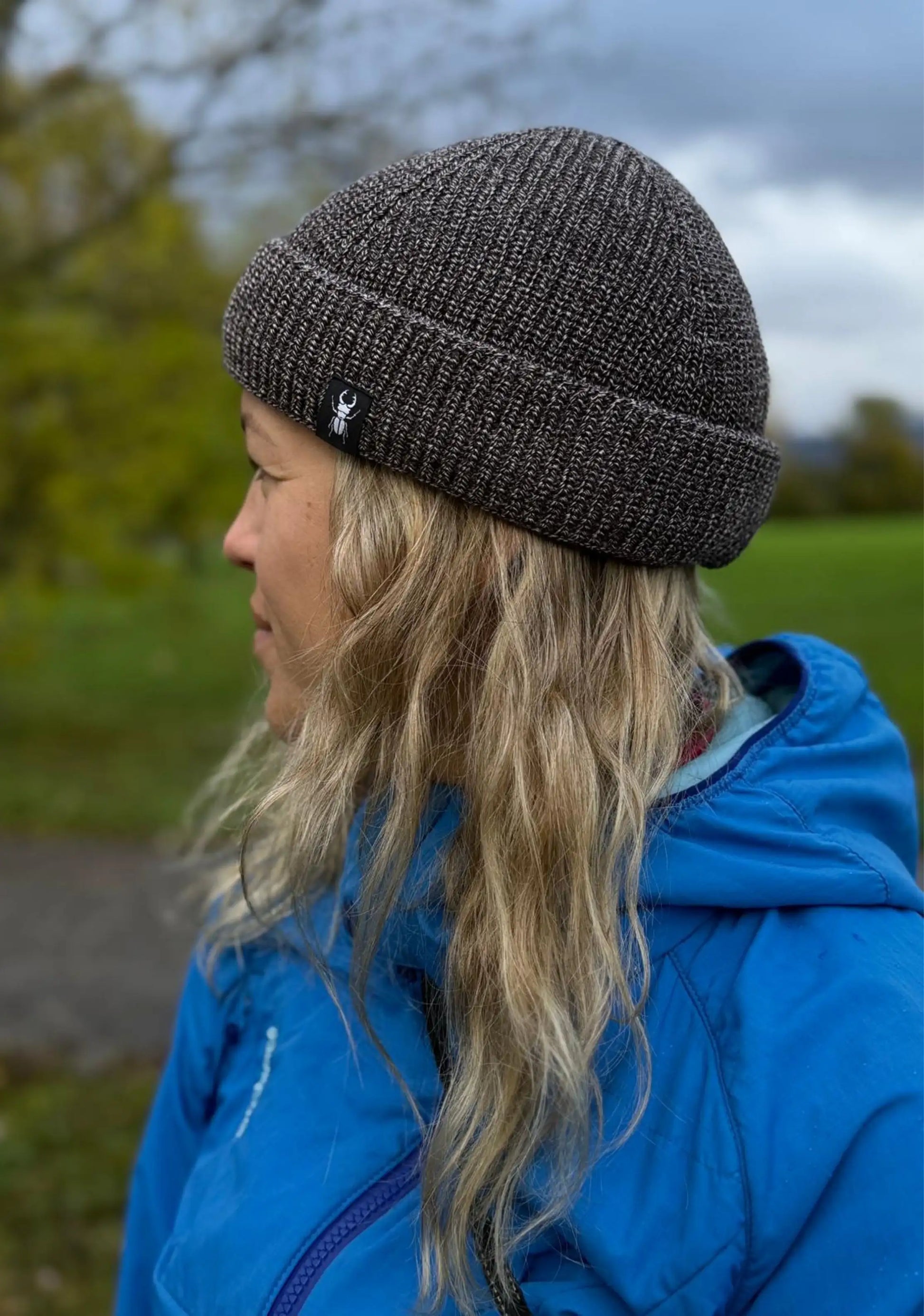 Frau mit langen blonden Haaren und blauer Jacke trägt Braun mellierte Fisherman Beanie von ArmyBug